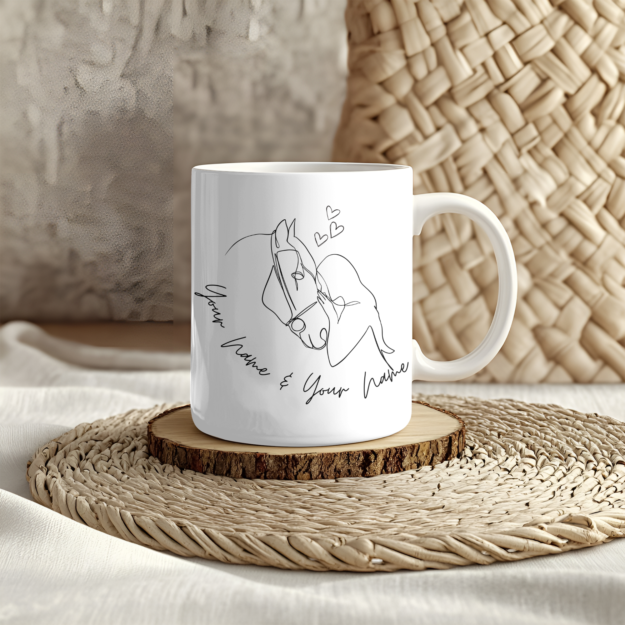 White mug featuring line art of two people kissing with small hearts above them, placed on a woven mat. The text below reads & your name & your name,&quot; making it perfect for adding a personalisierbar touch.